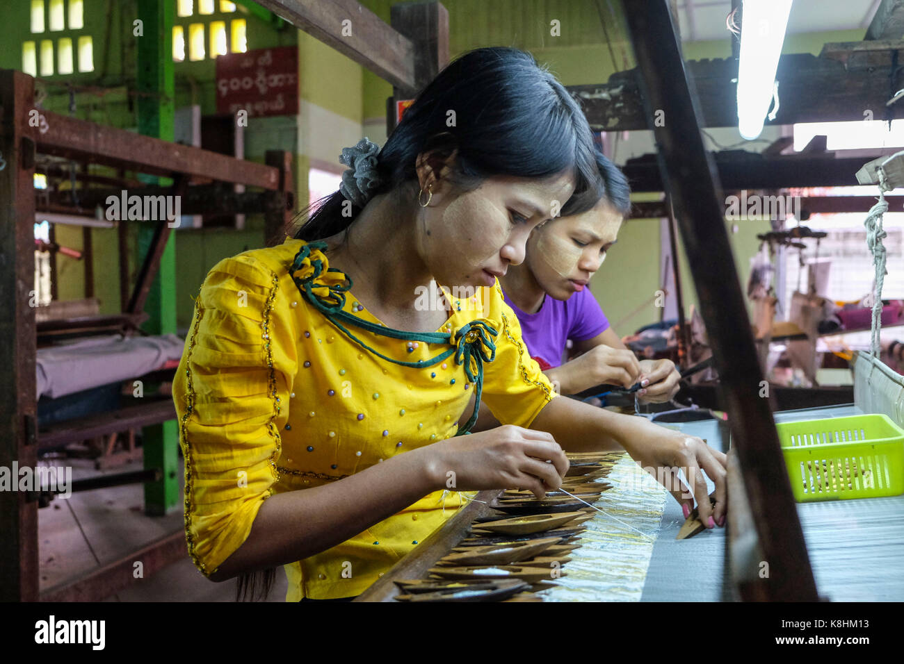 La Birmania, Myanmar Mandalay: laboratorio di tessitura. Le donne che lavorano nella parte anteriore di un telaio di tessitura: giovani donne, tessitori con Thanaka, giallo di un prodotto di bellezza, a t Foto Stock