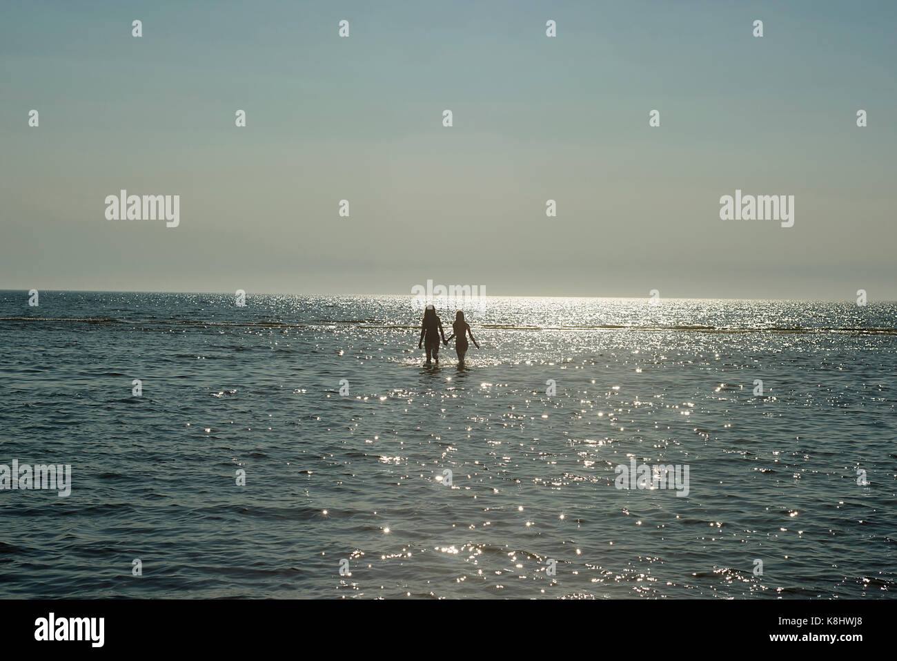 Silhouette a madre e figlia passeggiate in mare tenendo le mani contro sky Foto Stock