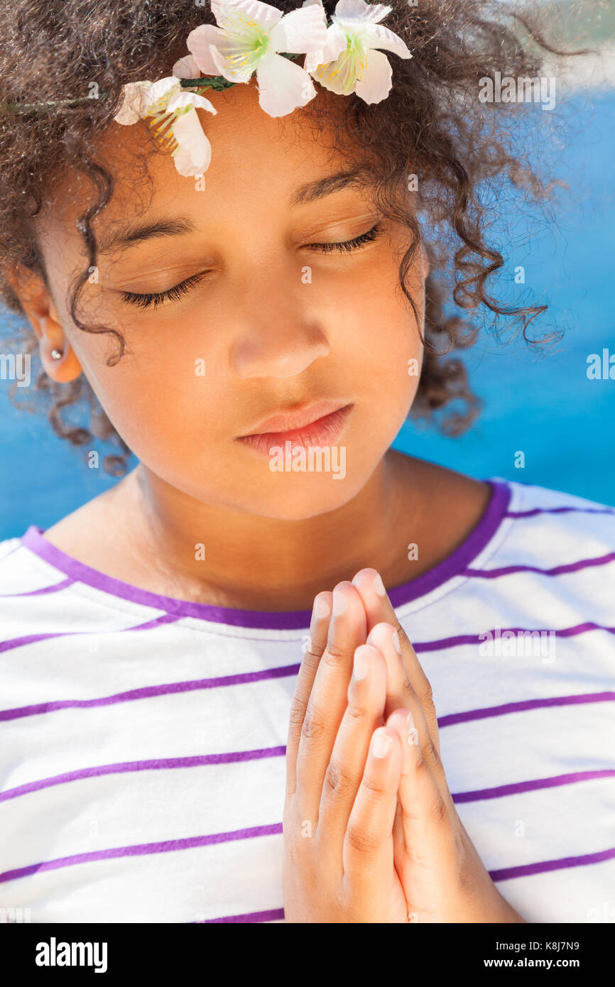 Angelic African American razza mista ragazza bambino gli occhi chiusi in preghiera pregando con fiori nei capelli Foto Stock