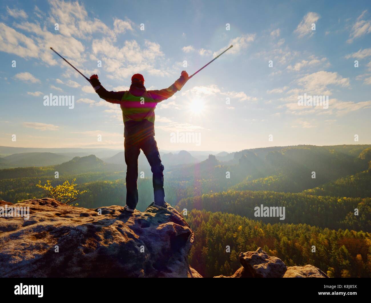 Turistico con avambraccio stampella sopra la testa sul sentiero. ferito escursionista raggiunto il picco di montagna con ginocchio rotti in immobilizzatore. profonda valle bellow silhouette o Foto Stock