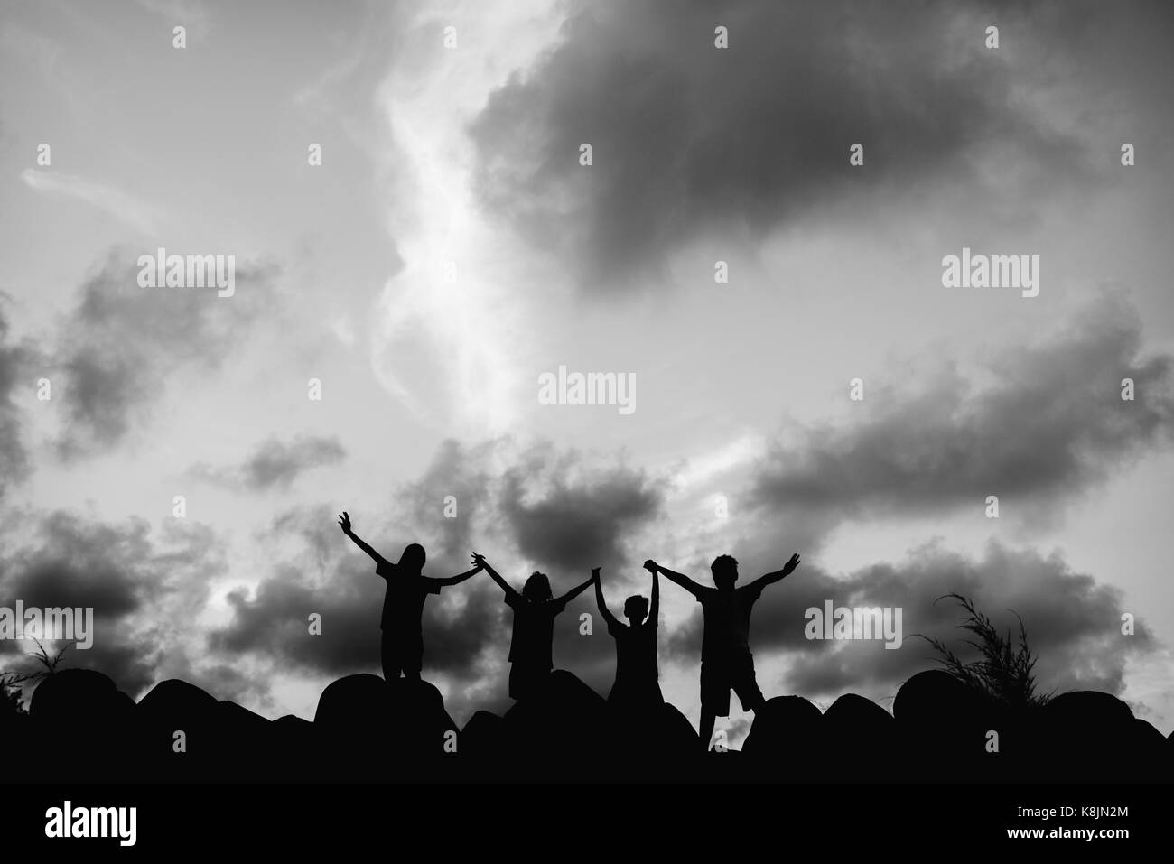 Silhouette foto di bambini in piedi su una pietra con ampio braccio aperto.contenti i bambini divertendosi insieme in silhouette.ombra di bambini in bianco e nero ph Foto Stock