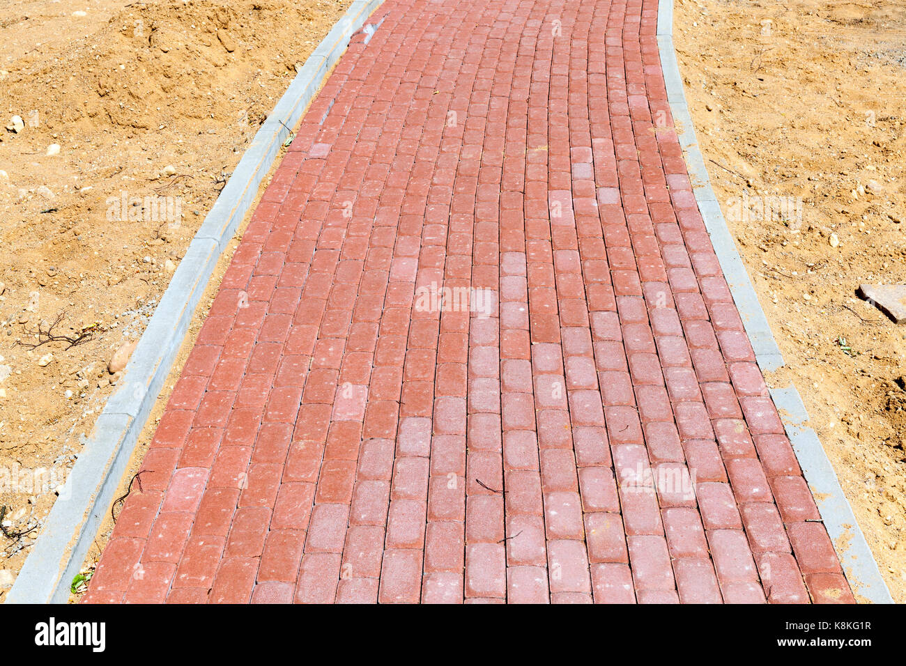 Una strada pedonale fatta di ciottoli di rosso. sabbia è stata versata lungo i bordi della pavimentazione del marciapiede. costruzione di infrastrutture in città Foto Stock