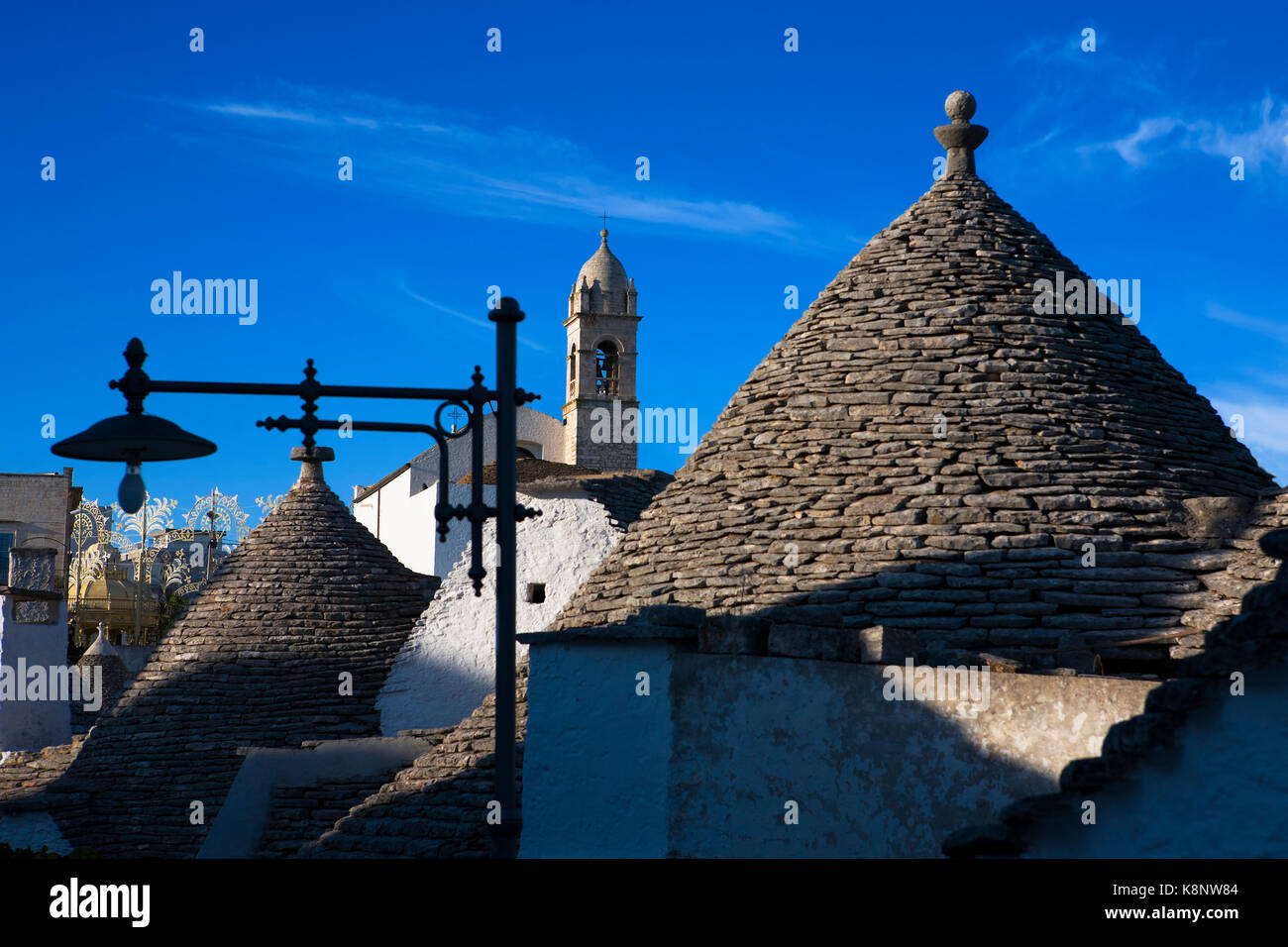 Tetti di Trulli, torre della chiesa e lam-post, Via Monte Nero, Rione Monti, Alberobello, Puglia' Italia Foto Stock