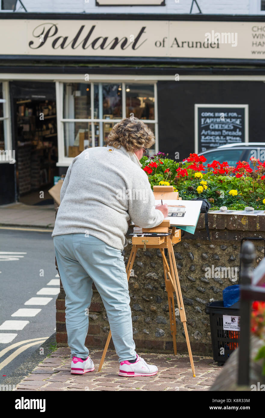 Artista femminile di verniciatura di un negozio locale utilizzando la vernice e un cavalletto in Arundel, West Sussex, in Inghilterra, Regno Unito. Foto Stock
