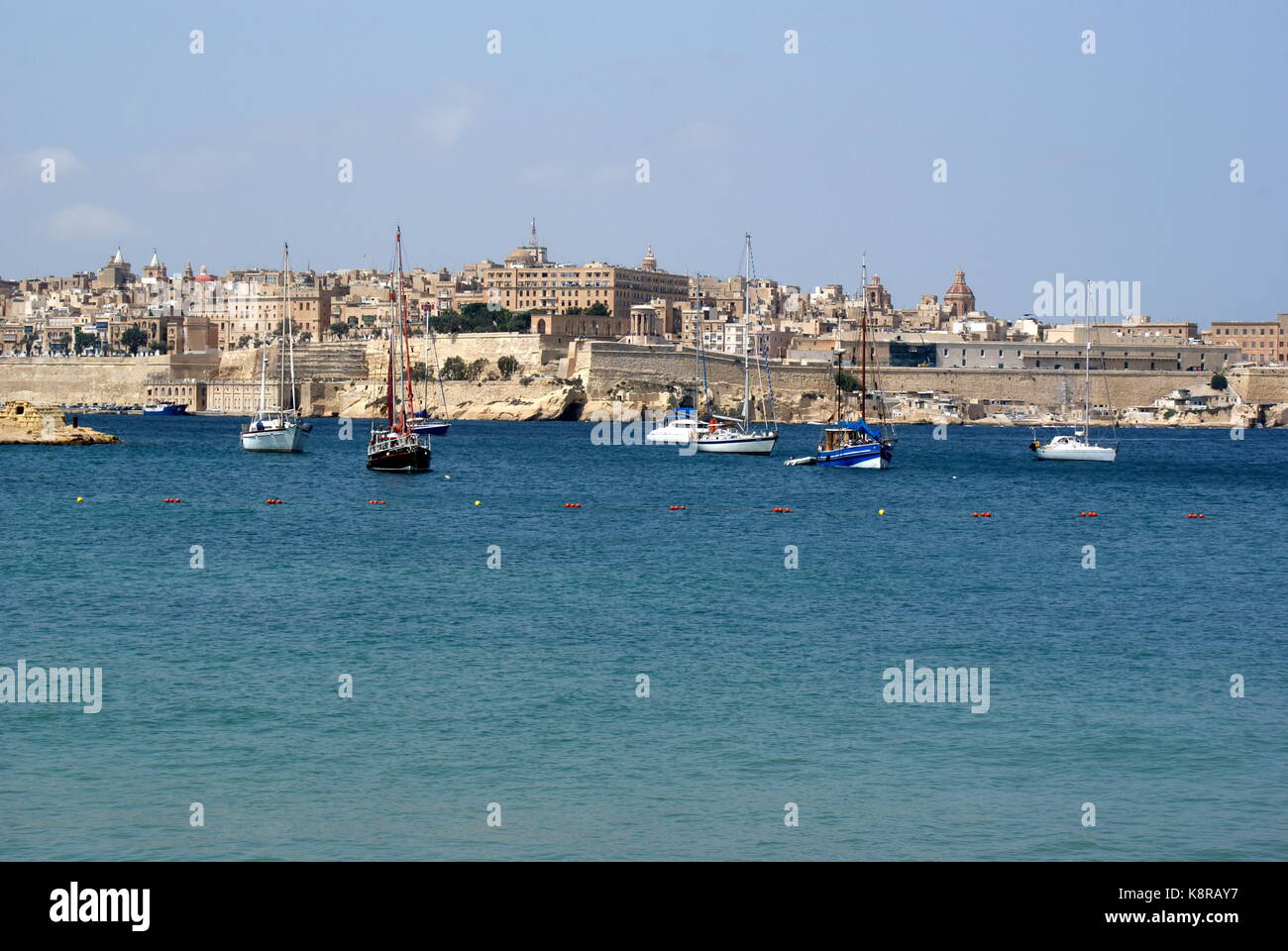 Barche a vela all'ancora nella baia di Rinella, Grand Harbour, di fronte alla città fortificata di Valletta, Malta Foto Stock