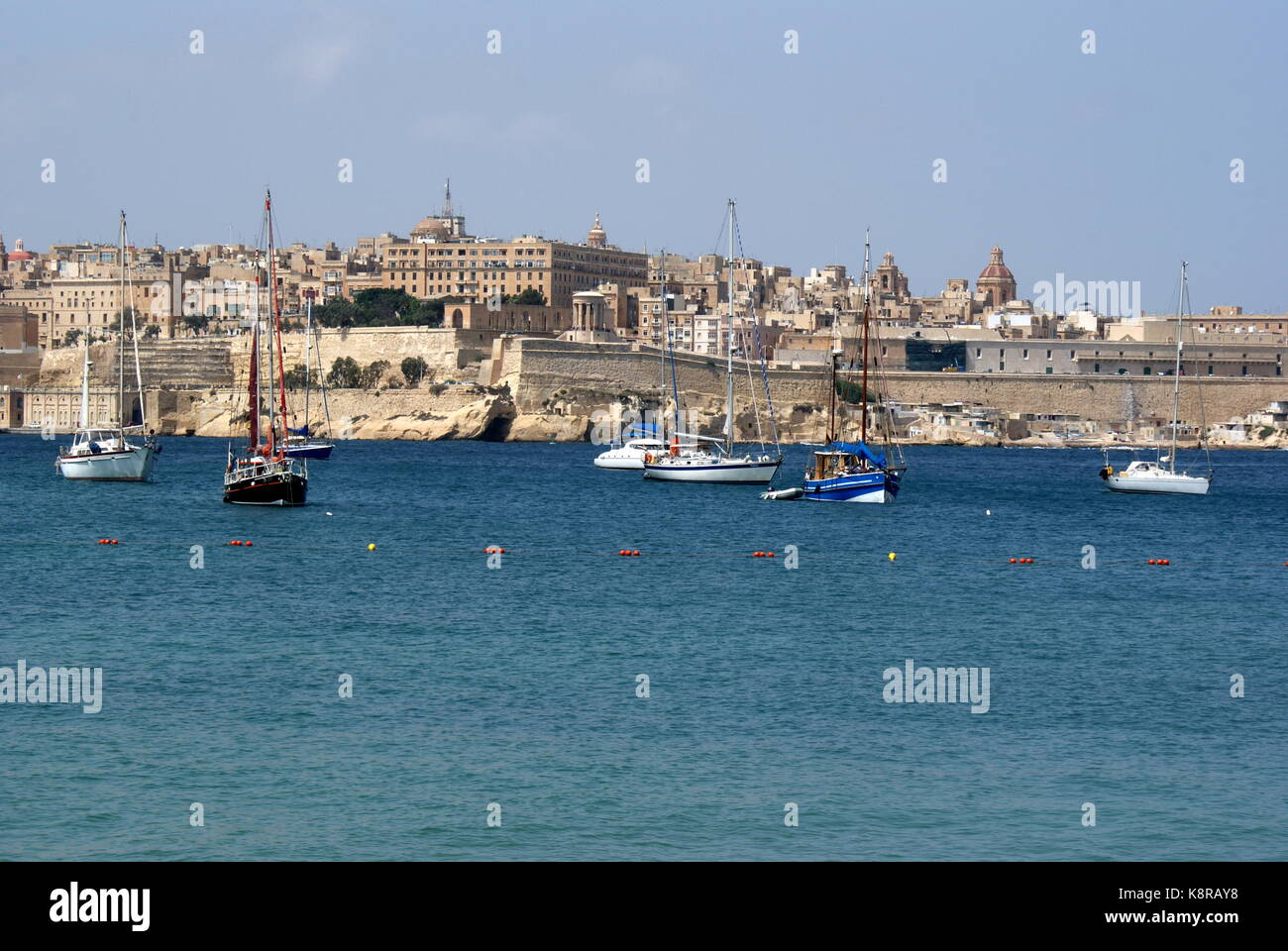 Barche a vela all'ancora nella baia di Rinella, Grand Harbour, di fronte alla città fortificata di Valletta, Malta Foto Stock