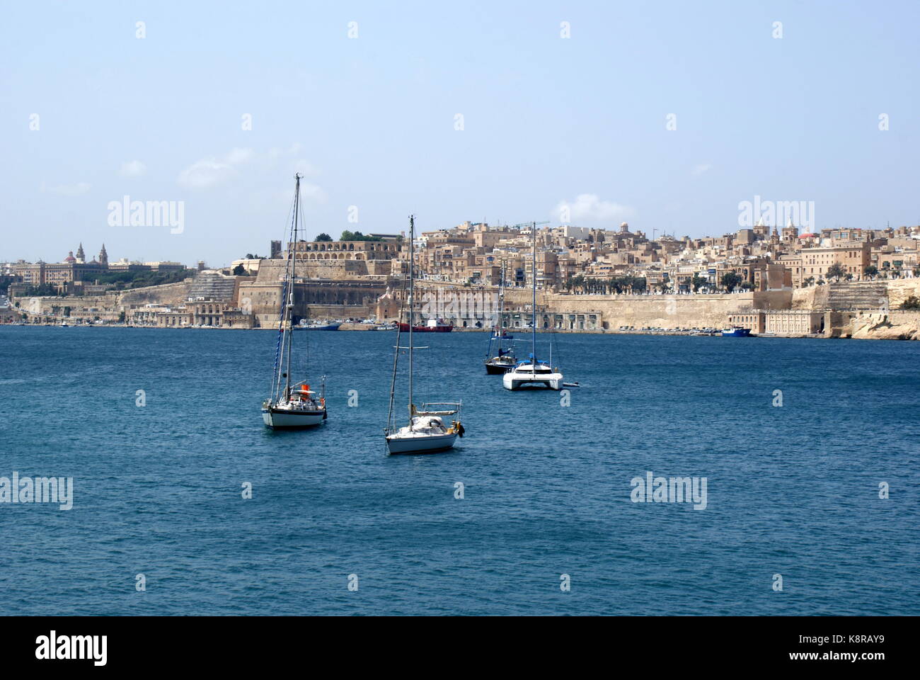 Barche a vela all'ancora nella baia di Rinella, Grand Harbour, di fronte alla città fortificata di Valletta, Malta Foto Stock