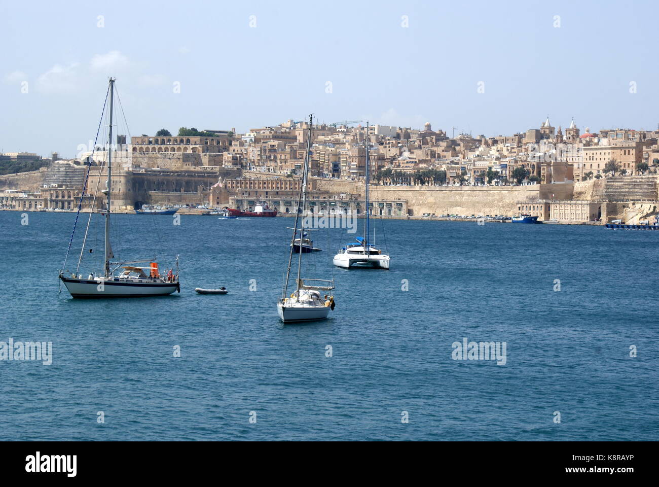 Barche a vela all'ancora nella baia di Rinella, Grand Harbour, di fronte alla città fortificata di Valletta, Malta Foto Stock