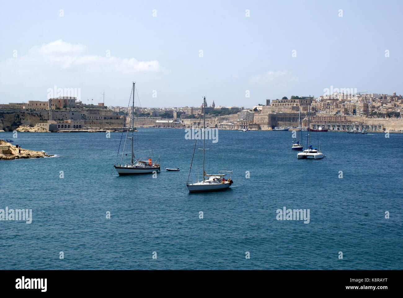 Barche a vela all'ancora nella baia di Rinella, Grand Harbour, di fronte alla città fortificata di Valletta, Malta Foto Stock