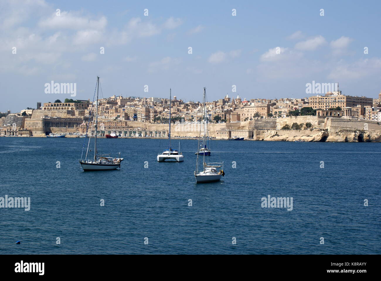 Barche a vela all'ancora nella baia di Rinella, Grand Harbour, di fronte alla città fortificata di Valletta, Malta Foto Stock