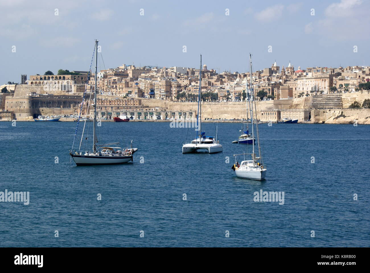 Barche a vela all'ancora nella baia di Rinella, Grand Harbour, di fronte alla città fortificata di Valletta, Malta Foto Stock