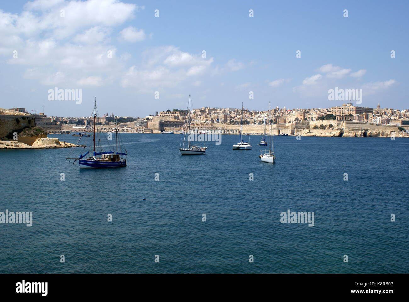 Barche a vela all'ancora nella baia di Rinella, Grand Harbour, di fronte alla città fortificata di Valletta, Malta Foto Stock