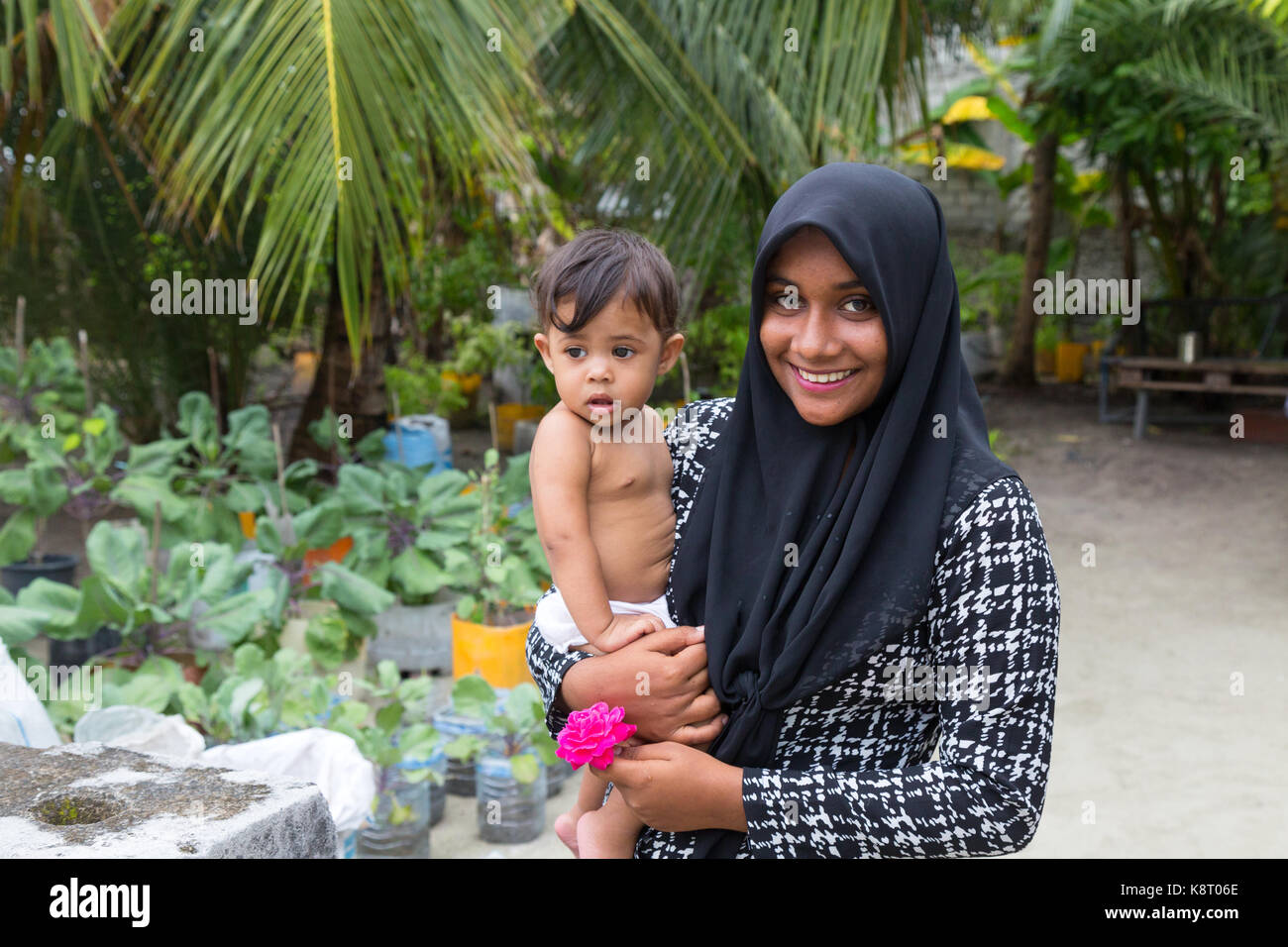 Maldive persone - un giovane Maldive asiatica donna musulmana di trasportare un bambino, Rasdhoo village, Maldive, Asia Foto Stock