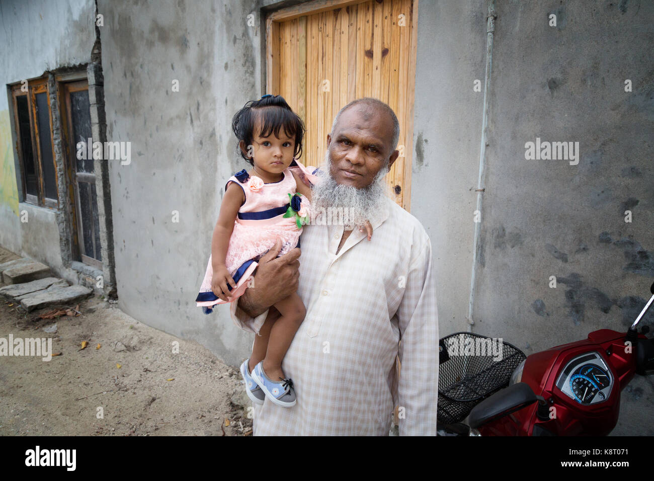 Maldive persone locali - e gli anziani uomo maldiviano di trasportare un bambino, rasdhoo island village, rasdhoo, Maldive, asia Foto Stock