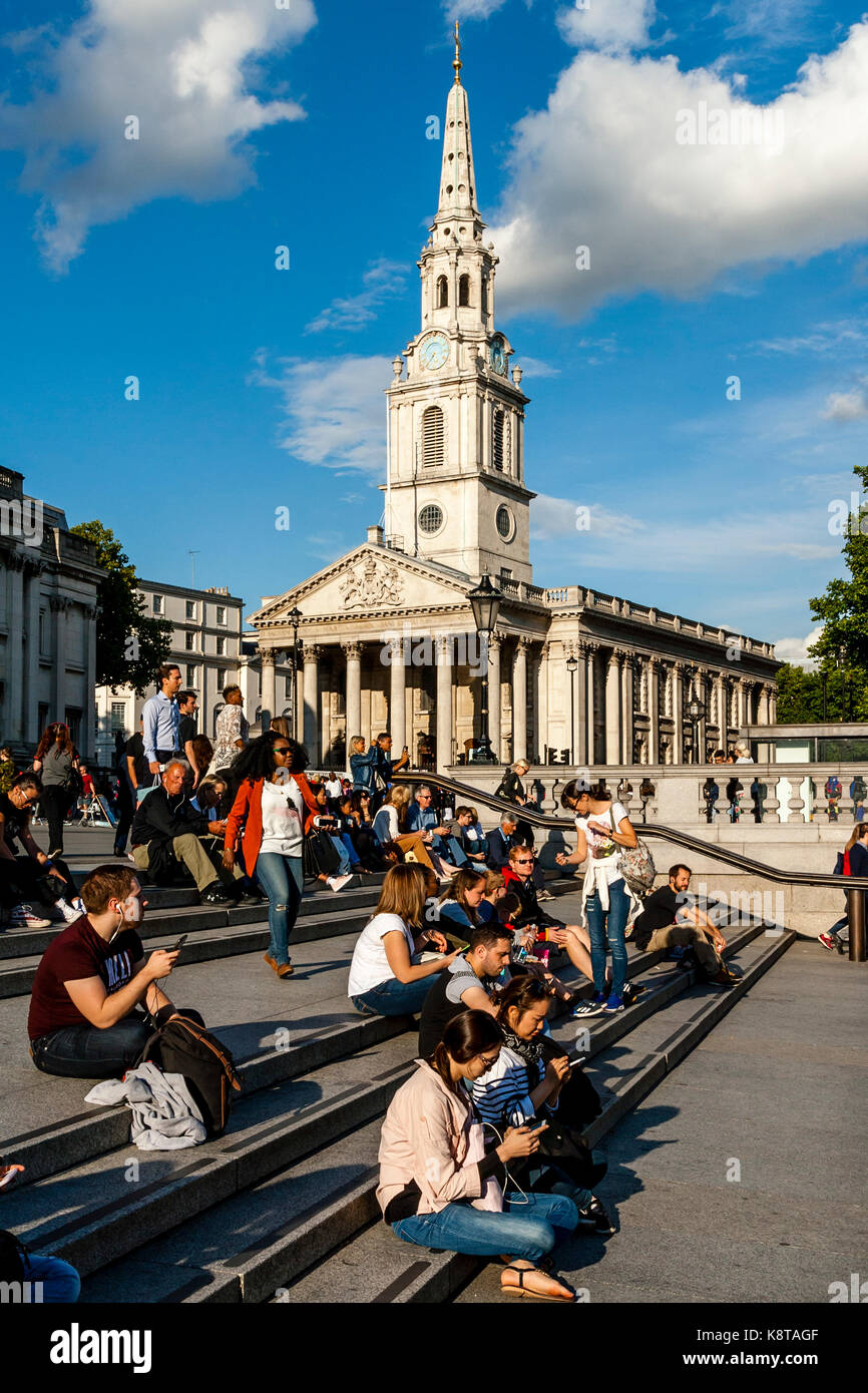 I giovani seduti sui gradini di Trafalgar Square con la chiesa di St Martin-in-the-Fields in backround, london, Regno Unito Foto Stock