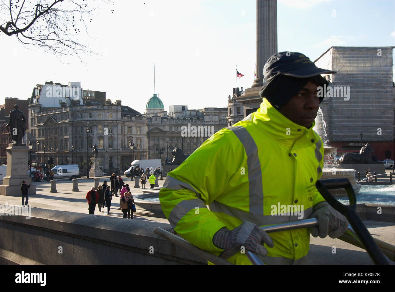 Un pulitore di via passeggiate fino il marciapiede attorno a Trafalgar Square. Foto Stock