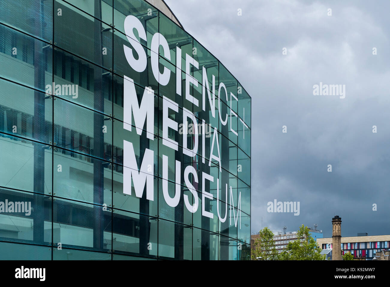 Grigio scuro sky & esterno della scienza e il Museo Multimediale (Bradford, West Yorkshire, Inghilterra, Regno Unito) - impressionante, curve, facciata vetrata & enorme nome sign. Foto Stock