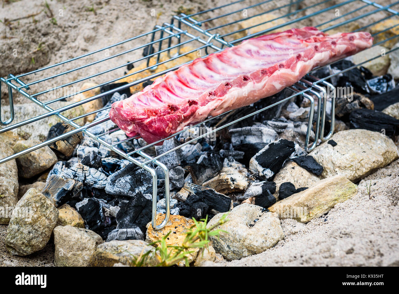 Rendendo costolette di maiale su fatti in casa barbecue improvvisato un barbecue. rendendo il churrasco su un carbone, incendio, bricchetti barbecue nella sabbia con pietre e sassi o Foto Stock