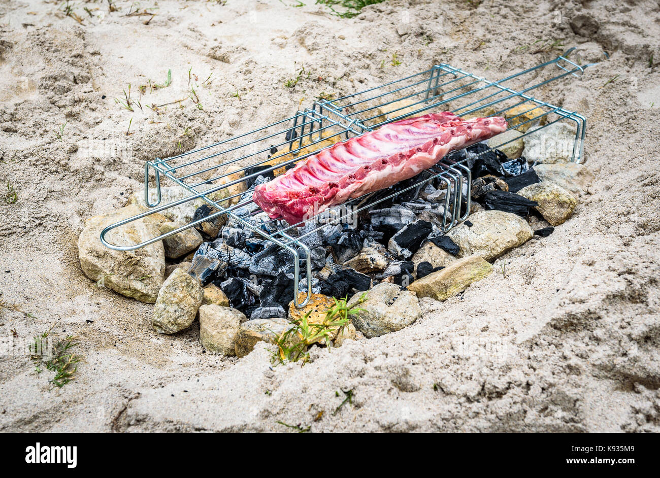 Rendendo costolette di maiale su fatti in casa barbecue improvvisato un barbecue. rendendo il churrasco su un carbone, incendio, bricchetti barbecue nella sabbia con pietre e sassi c Foto Stock