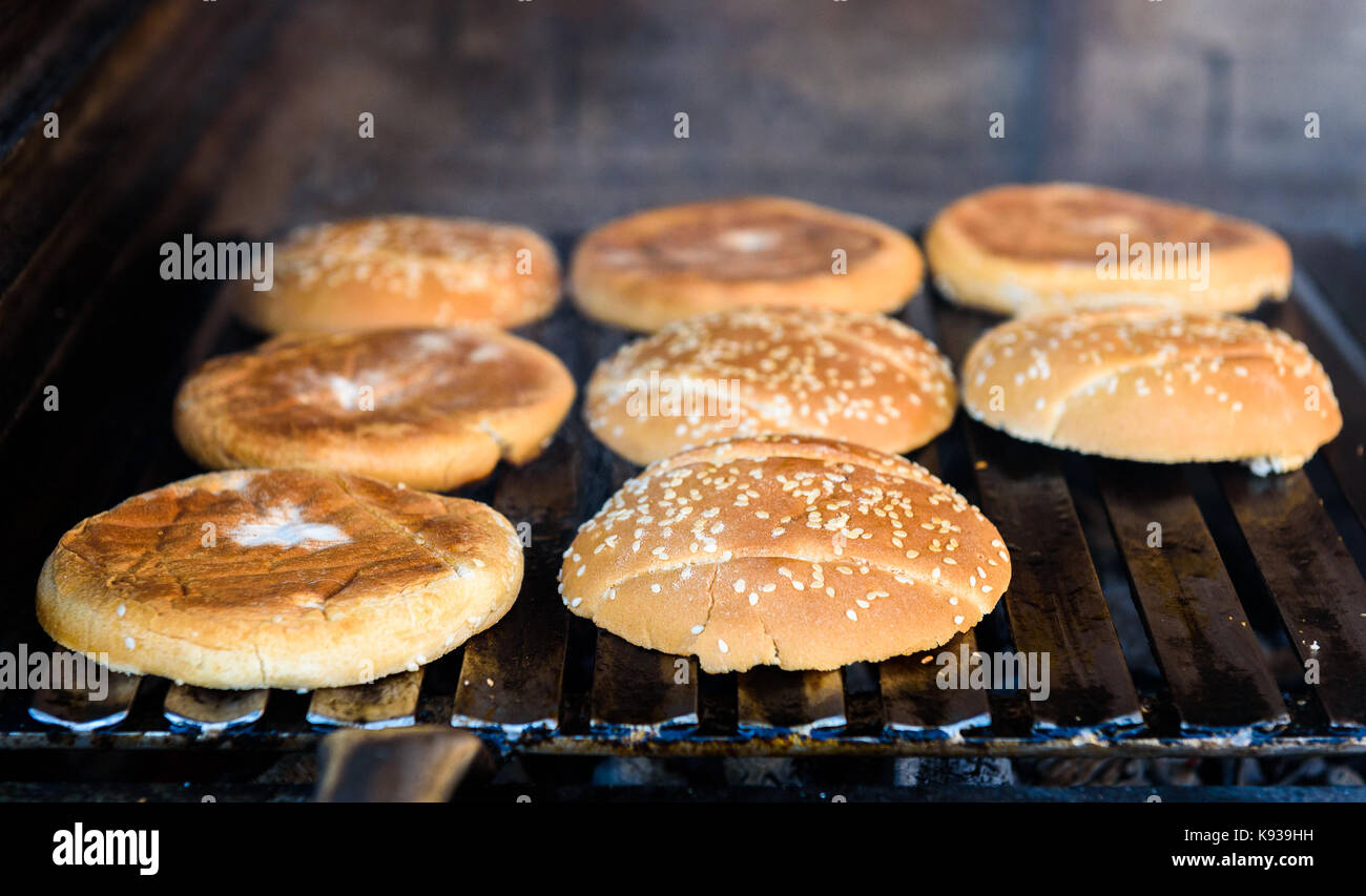 Facendo e grigliare panini hamburger con sesamo sulla griglia a carbone. preparazione di cibi arrosto su barbecue grill barbecue nel caminetto all'aperto e a forma di u griglia fuoco. Foto Stock