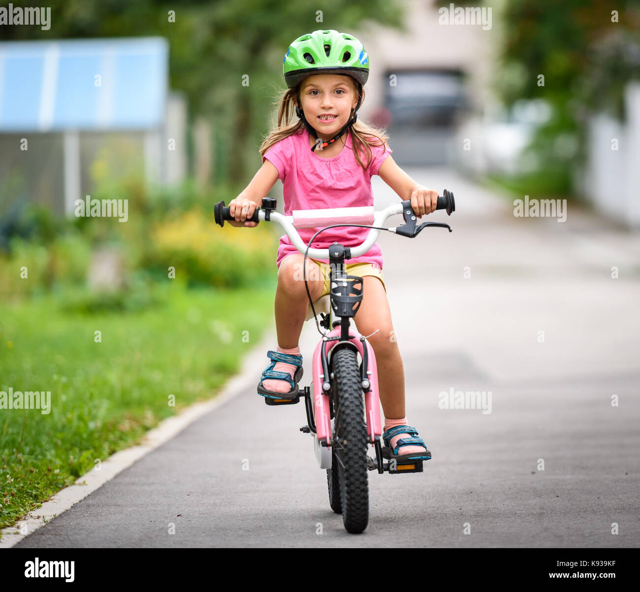 I bambini ad imparare a guidare una bicicletta su un vialetto esterno.  bambine equitazione biciclette su strada asfaltata in città che indossa  caschi protettivi come ingranaggio Foto stock - Alamy