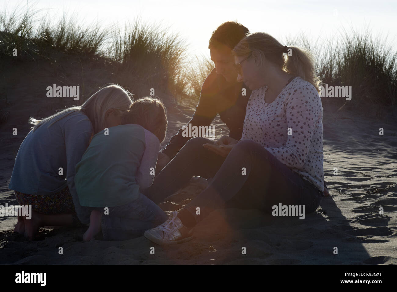 Una famiglia seduta sulle dune di sabbia guardando i serbatoi al tramonto. Foto Stock