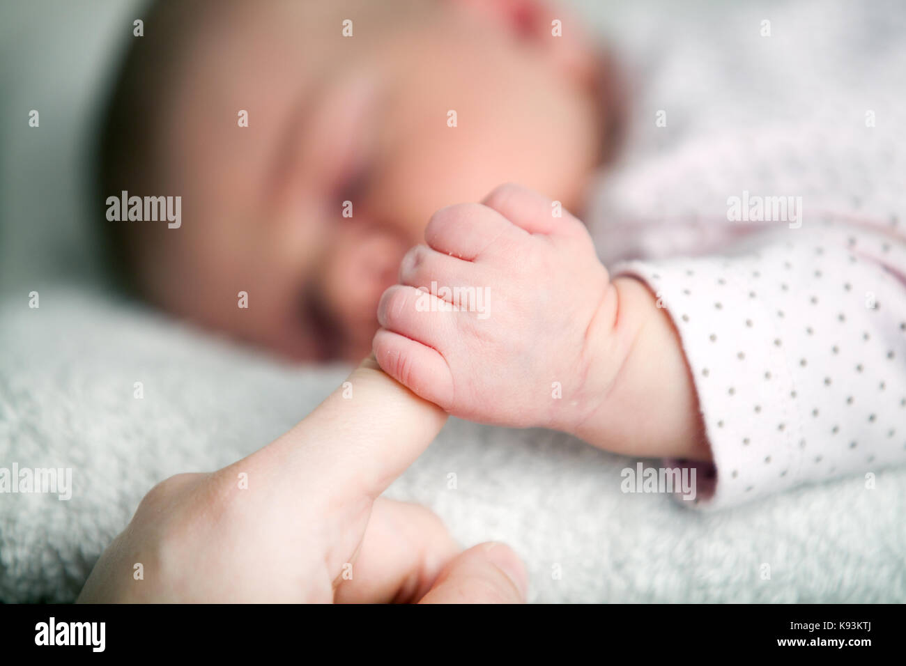 Un bambino molto giovane, sdraiato, e teso fuori per afferrare le sue mamme dito con la sua mano minuscola. Foto Stock
