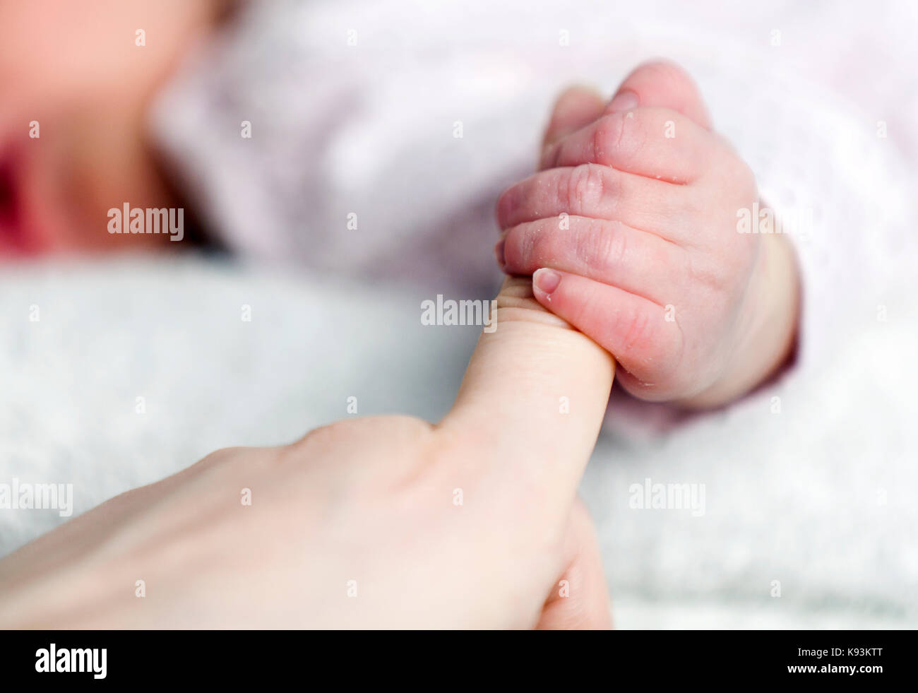 Un bambino molto giovane, sdraiato, e teso fuori per afferrare le sue mamme dito con la sua mano minuscola. Foto Stock