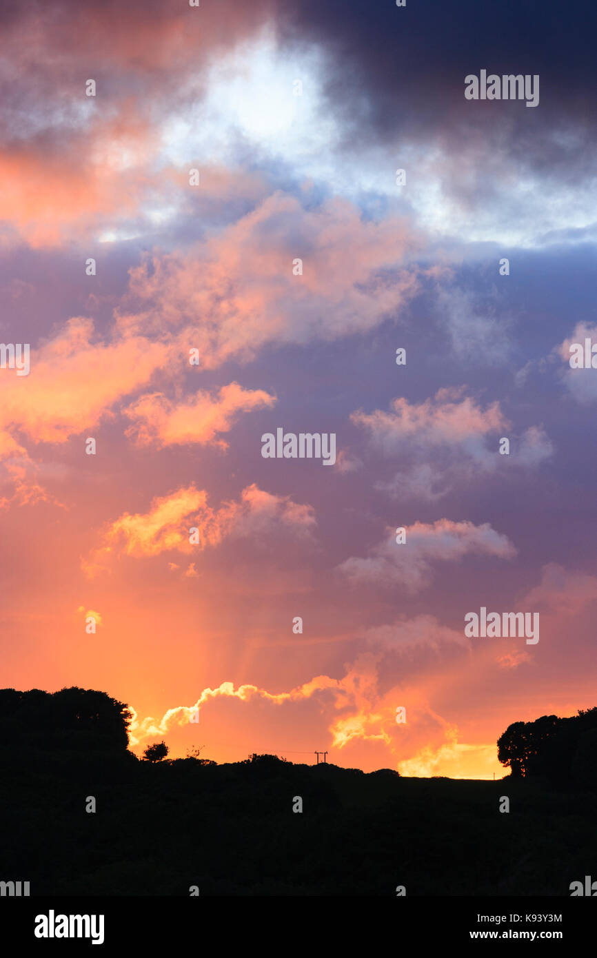 Arancio brillante tramonto illumina le nuvole sopra la silhouette di un Cornish Hillside Foto Stock