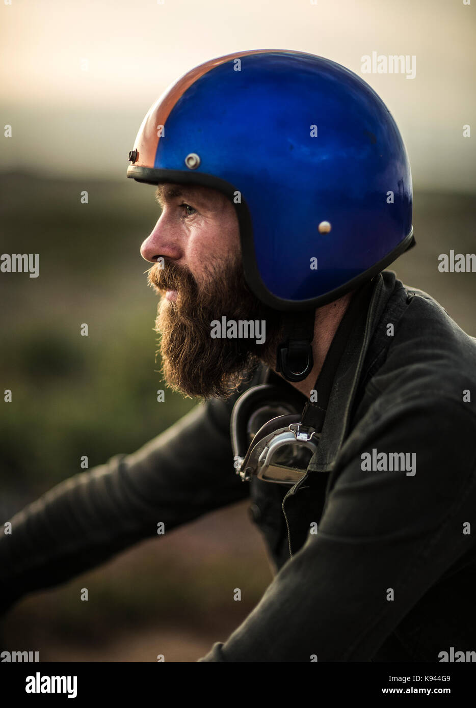 Profilo di uomo barbuto indossando blue faccia aperta casco, occhiali di protezione intorno al suo collo. Foto Stock