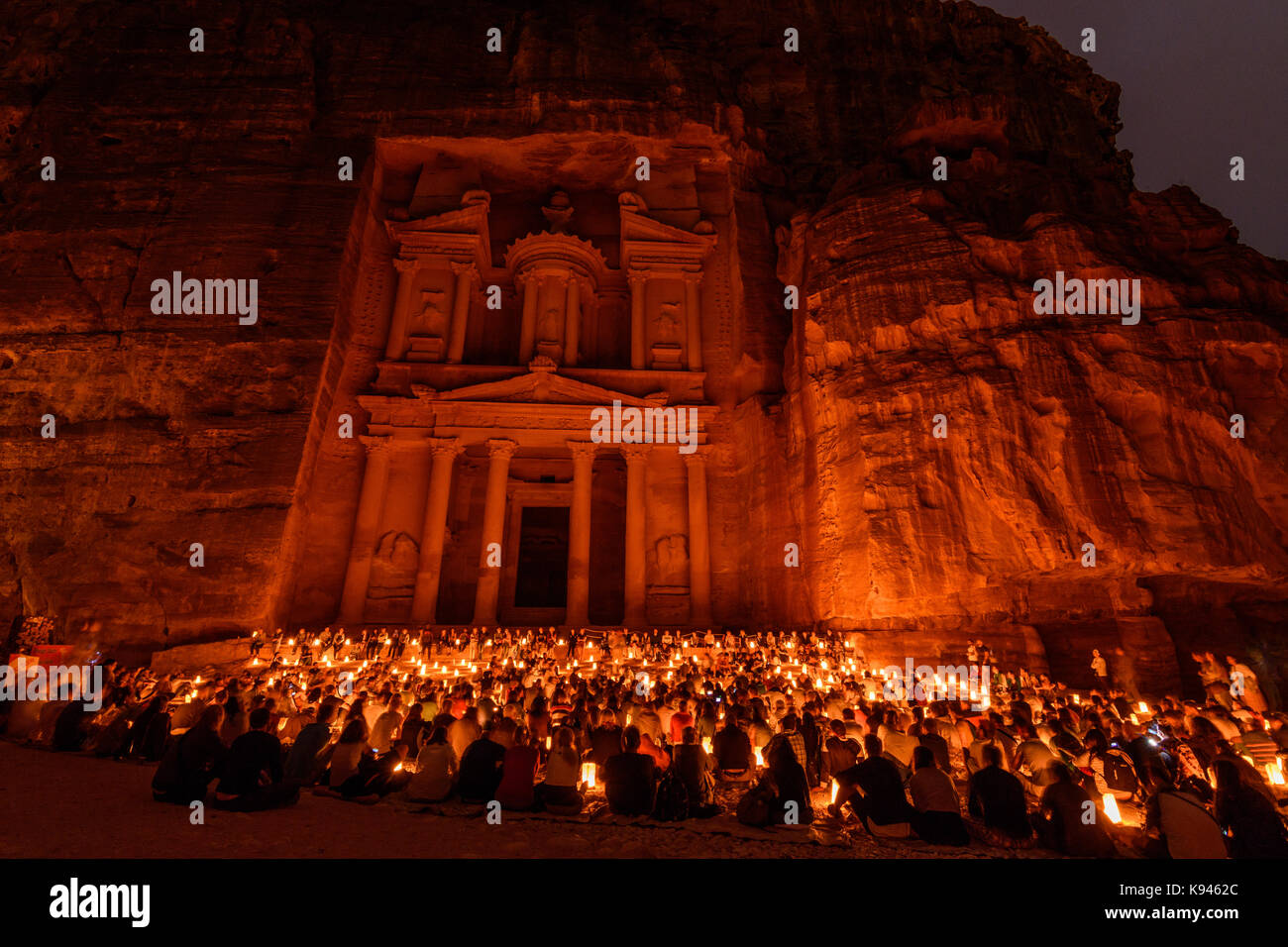 Vista esterna del rock-cut architettura di al khazneh o del tesoro di Petra, Giordania con un grande gruppo di persone sedute a terra di notte. Foto Stock