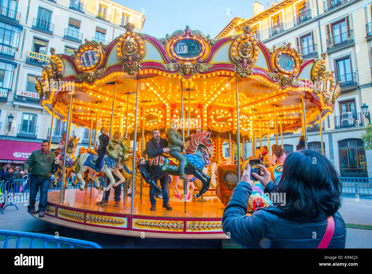 Donna di scattare le foto della sua famiglia a giostra. Plaza Santa Cruz, Madrid, Spagna. Foto Stock