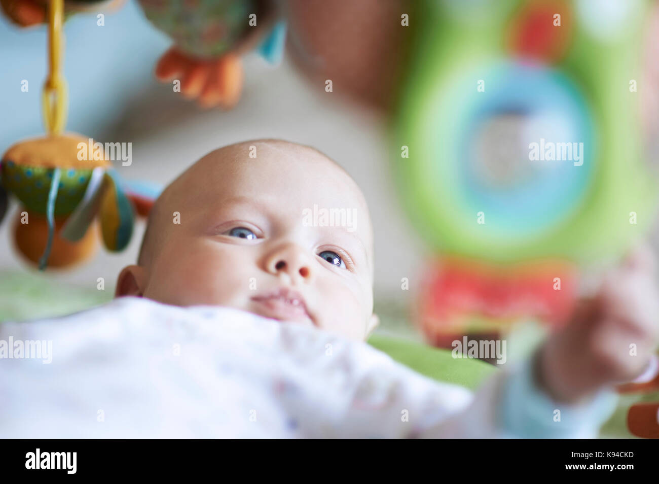 Close-up verticale di un giovanissimo neonato bimbo avvolto in bianche fresche vestiti del bambino circondato dai suoi giocattoli mobili colorati e riprodurre le cose. Foto Stock