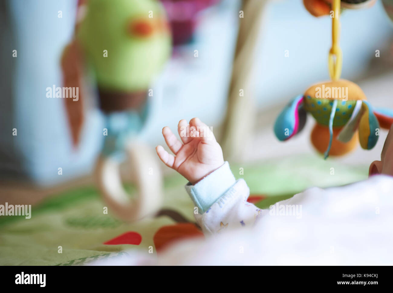 Close-up verticale di un giovanissimo neonato bimbo a corpo e braccio avvolto in bianche fresche vestiti del bambino come egli si allunga per i suoi giocattoli che sono a colori Foto Stock
