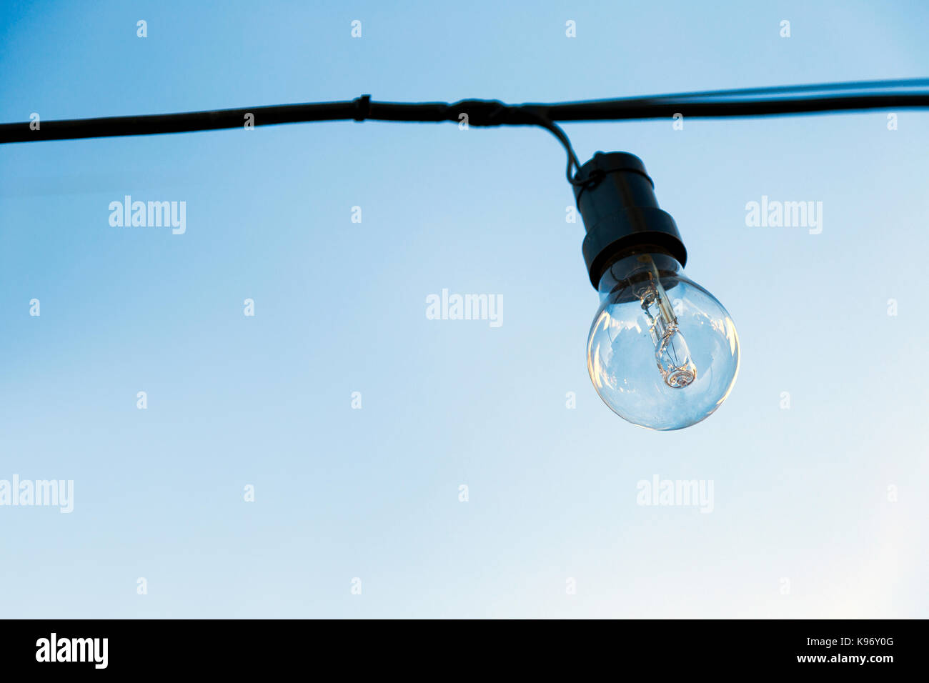 Una lampadina spenta, appesa a un cavo all'esterno. Il cielo blu sullo sfondo. Foto Stock