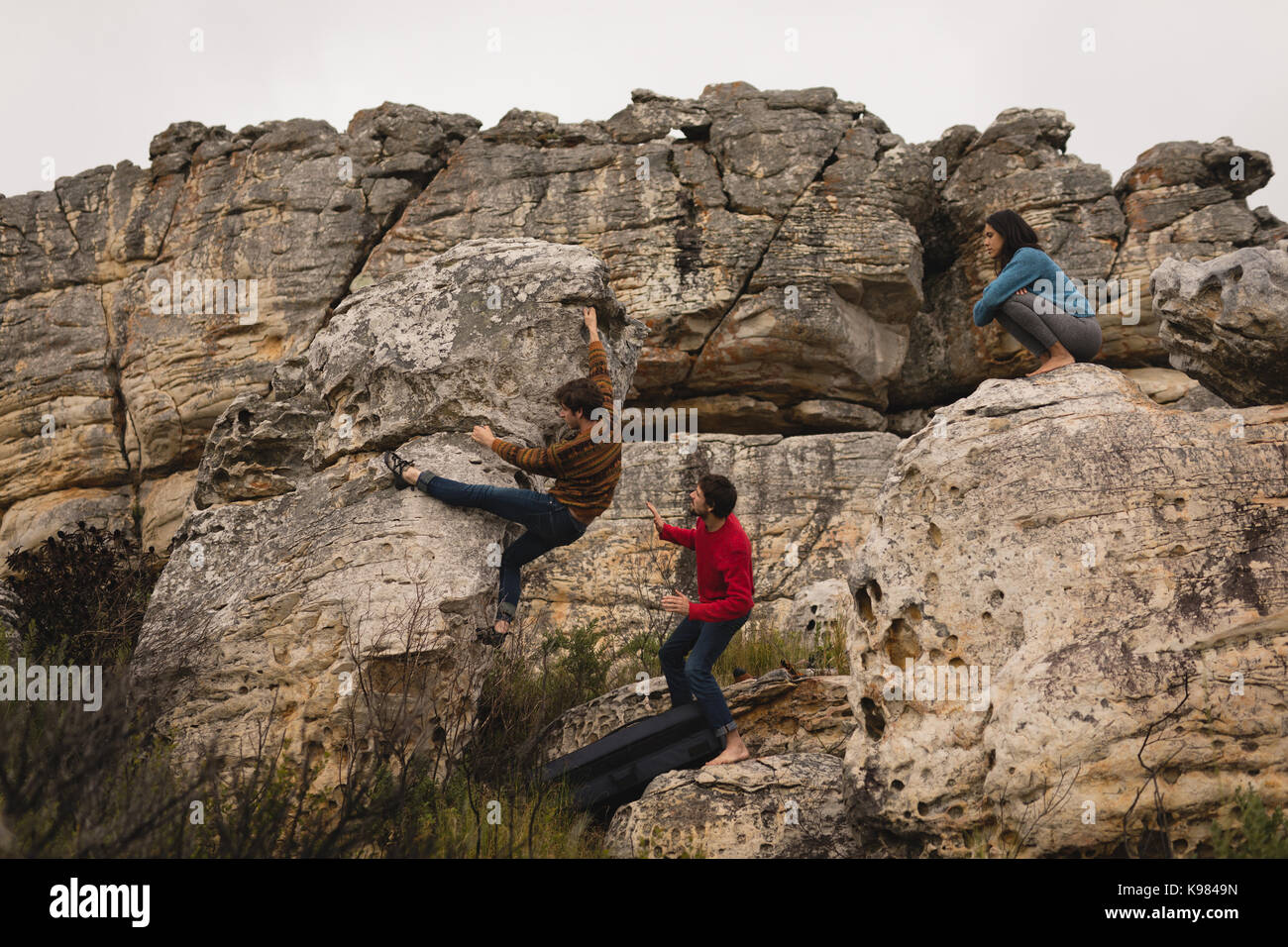 Gli amici di assistere l'uomo in arrampicata su roccia in una giornata di sole Foto Stock