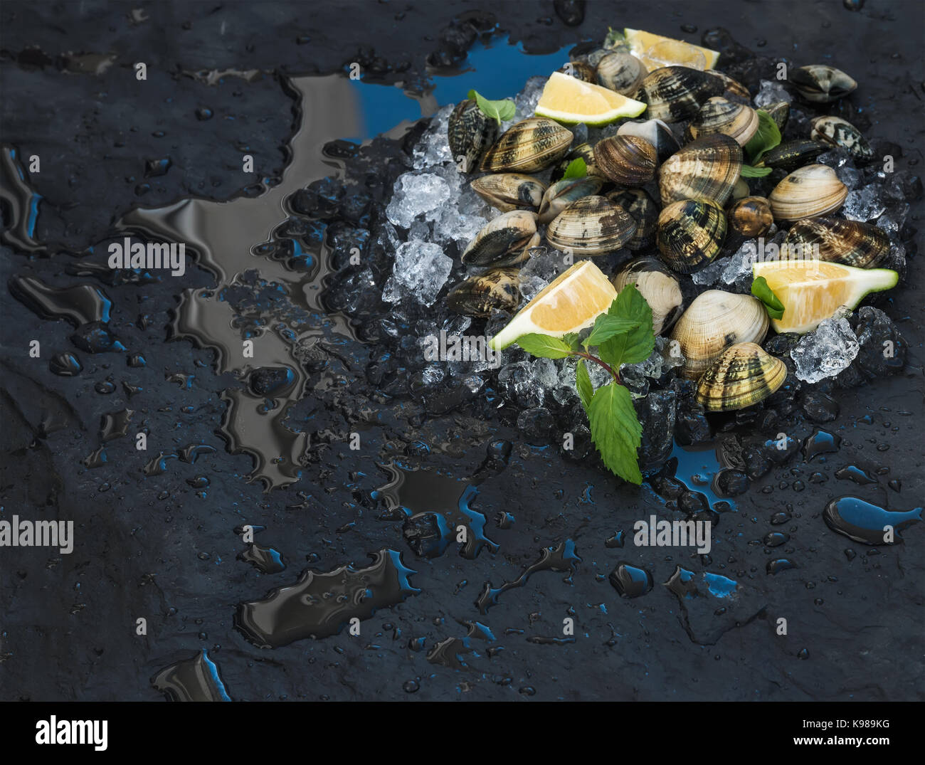 Non cotte fresche le vongole con il limone, erbe aromatiche e spezie sul ghiaccio scheggiata su ardesia scura sullo sfondo di pietra Foto Stock