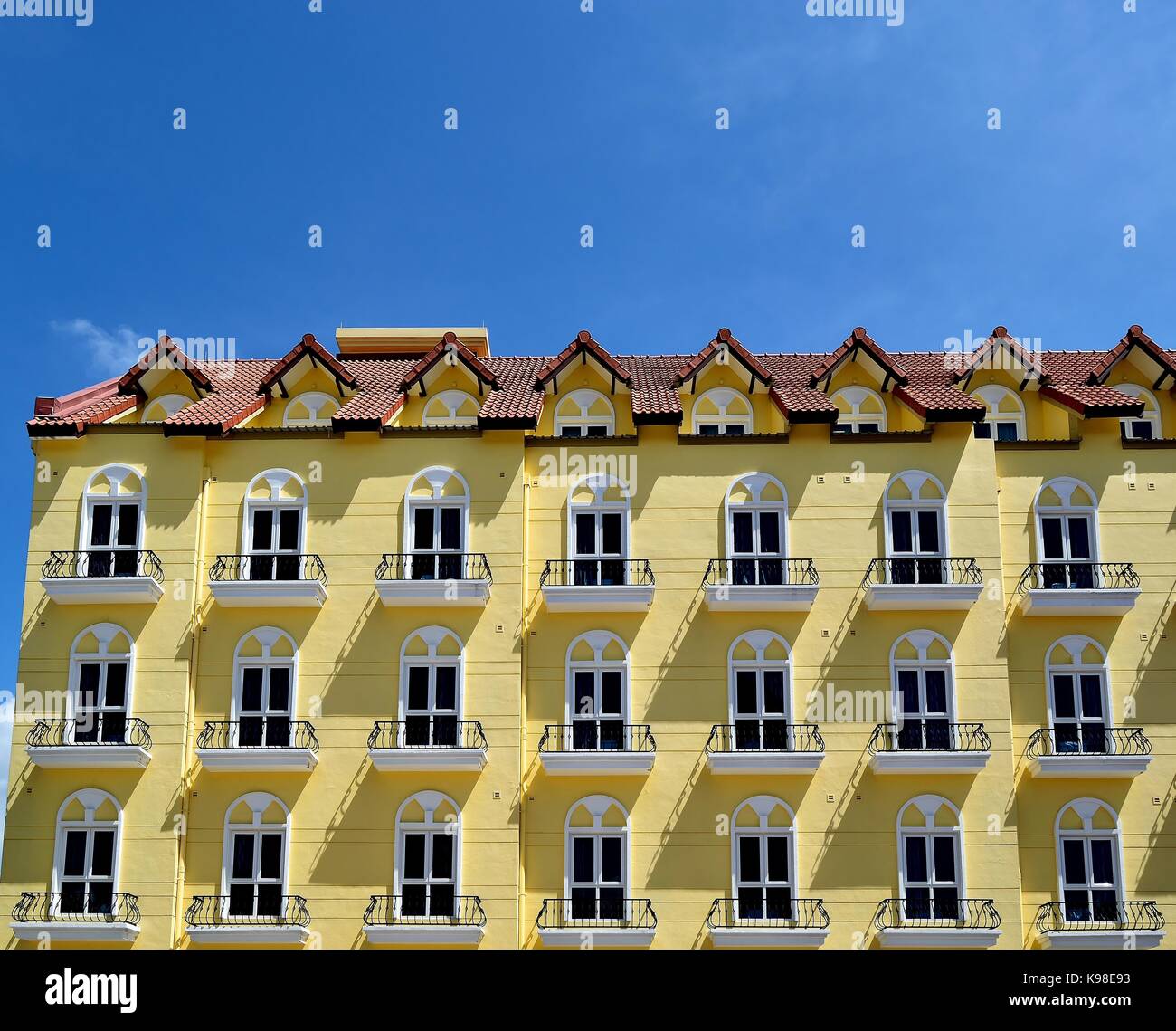 Una facciata classica di una residenza signorile in Singapore con giallo luminoso esterno, balconi di ferro e ombre spettacolari set contro un profondo blu del cielo tropicale Foto Stock