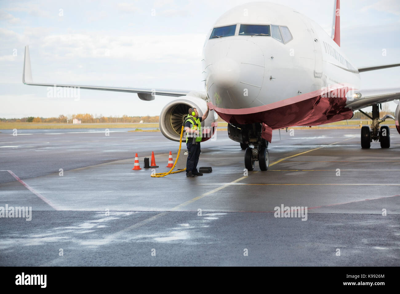 Lavoratore aereo di carica su bagnato pista di aeroporto Foto Stock