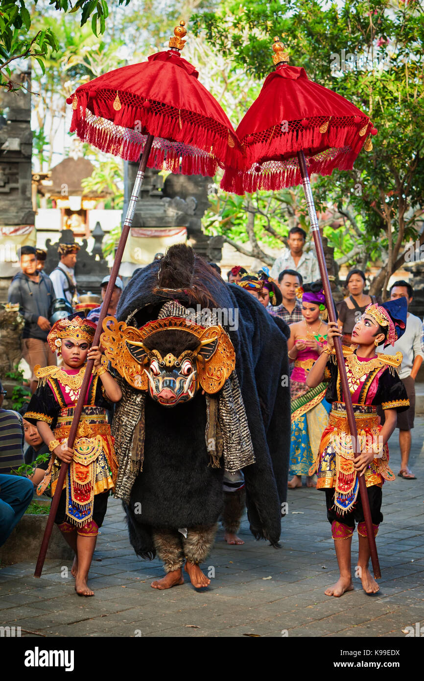 Bali, Indonesia - 21 giugno 2015: ballerini in costumi etnici a piedi sotto gli ombrelloni con gli uomini in maschera tradizionale balinese di buono spirito barong Foto Stock