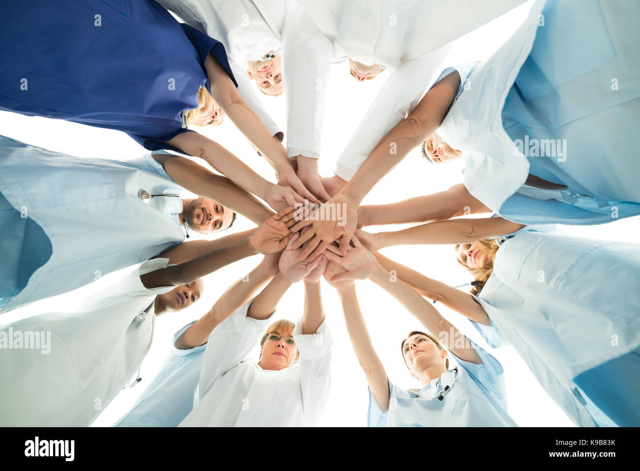 Direttamente sotto il tiro della società multietnica il team medico di mani di impilamento su sfondo bianco Foto Stock