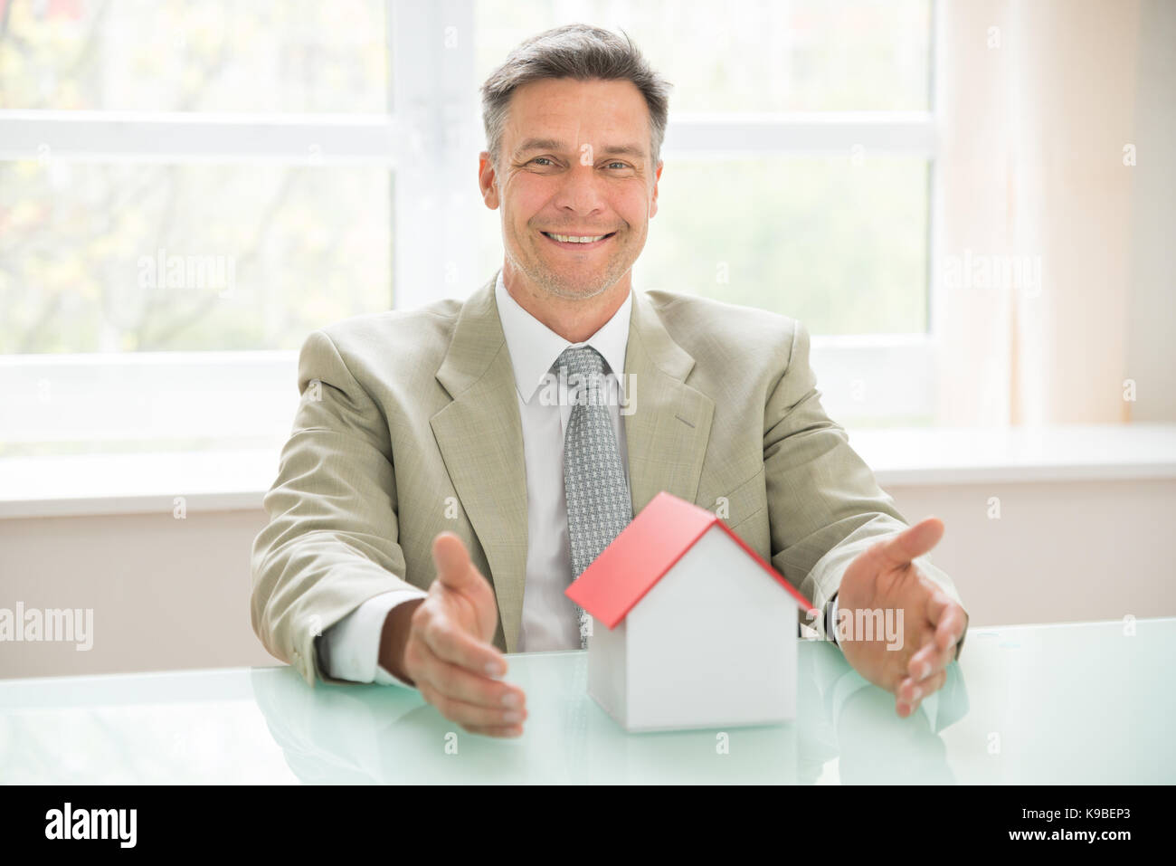 Ritratto di un happy businessman con modello di casa sulla scrivania Foto Stock
