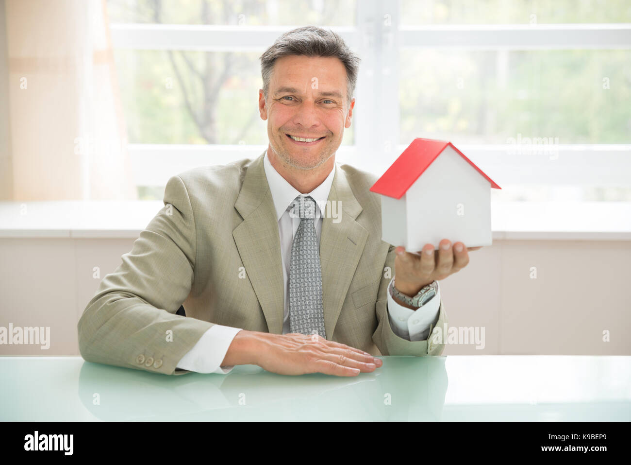 Ritratto di un happy businessman holding modello di casa in ufficio Foto Stock
