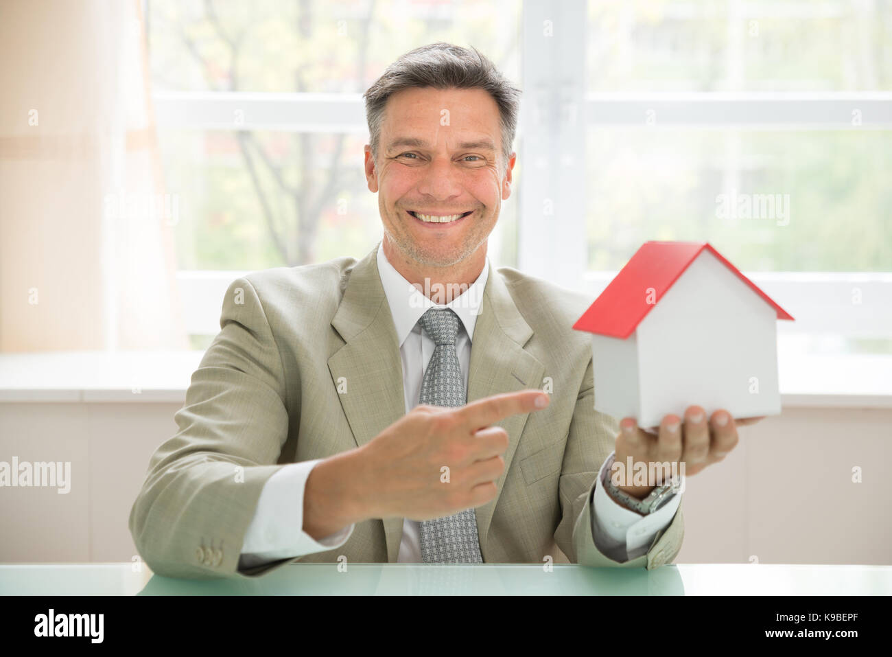 Ritratto di un happy businessman holding modello di casa in ufficio Foto Stock
