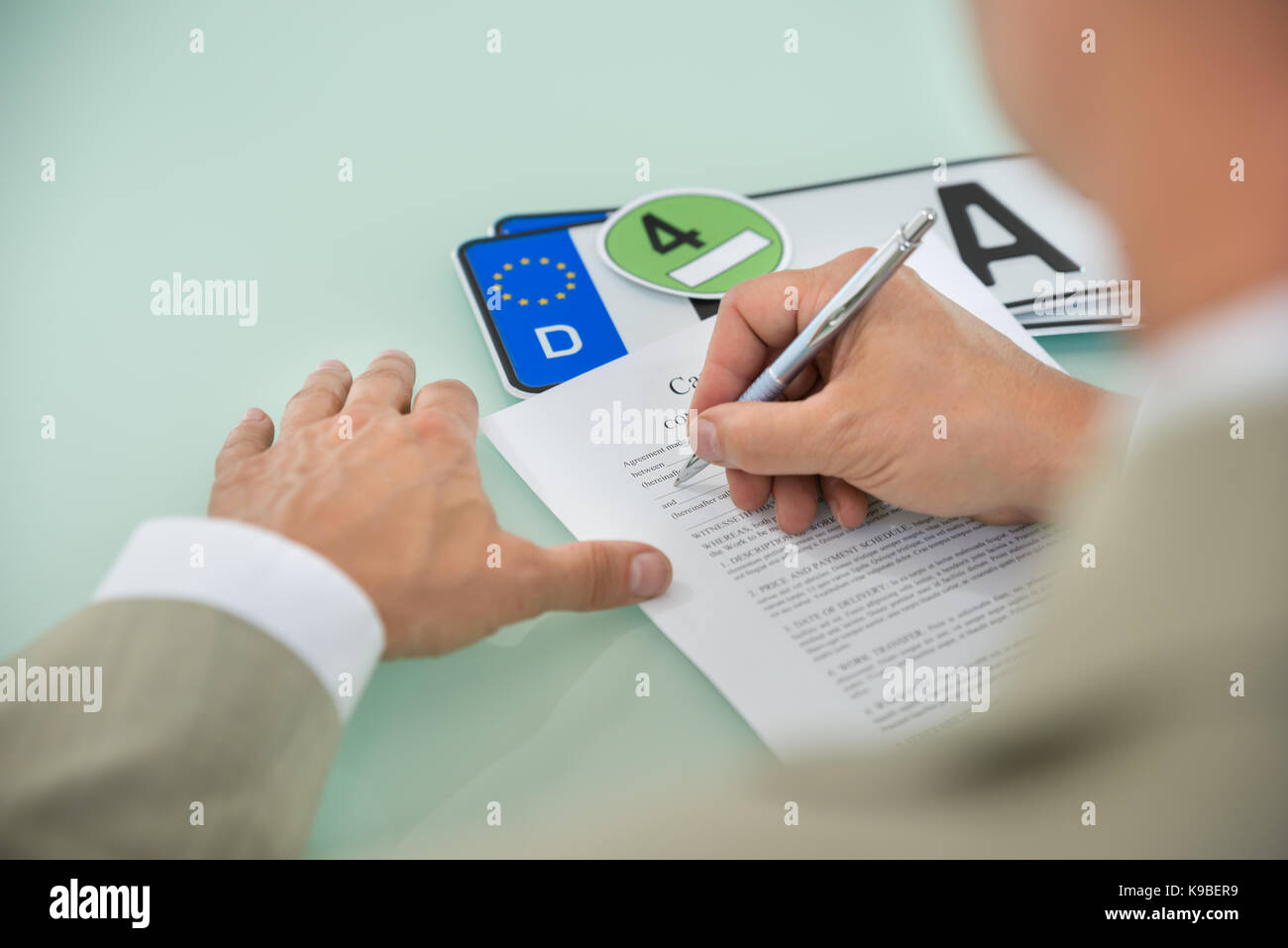 Close-up di un imprenditore di riempimento vendita auto modulo di contratto con targa automobilistica sulla scrivania. contratto la carta contiene il testo segnaposto Foto Stock