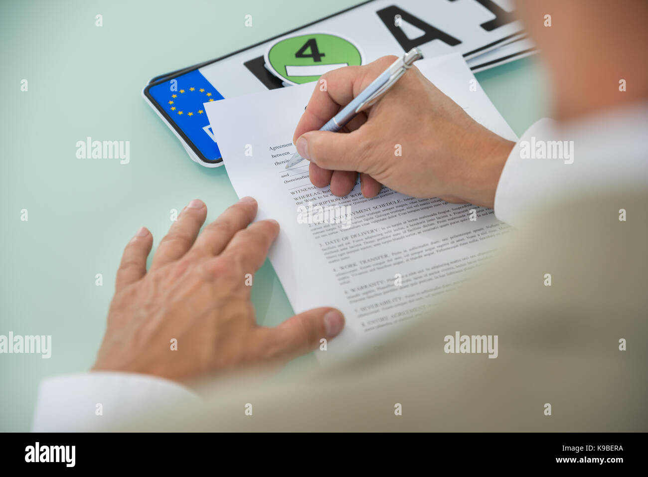 Close-up di un imprenditore di riempimento vendita auto modulo di contratto con targa automobilistica sulla scrivania. contratto la carta contiene il testo segnaposto Foto Stock