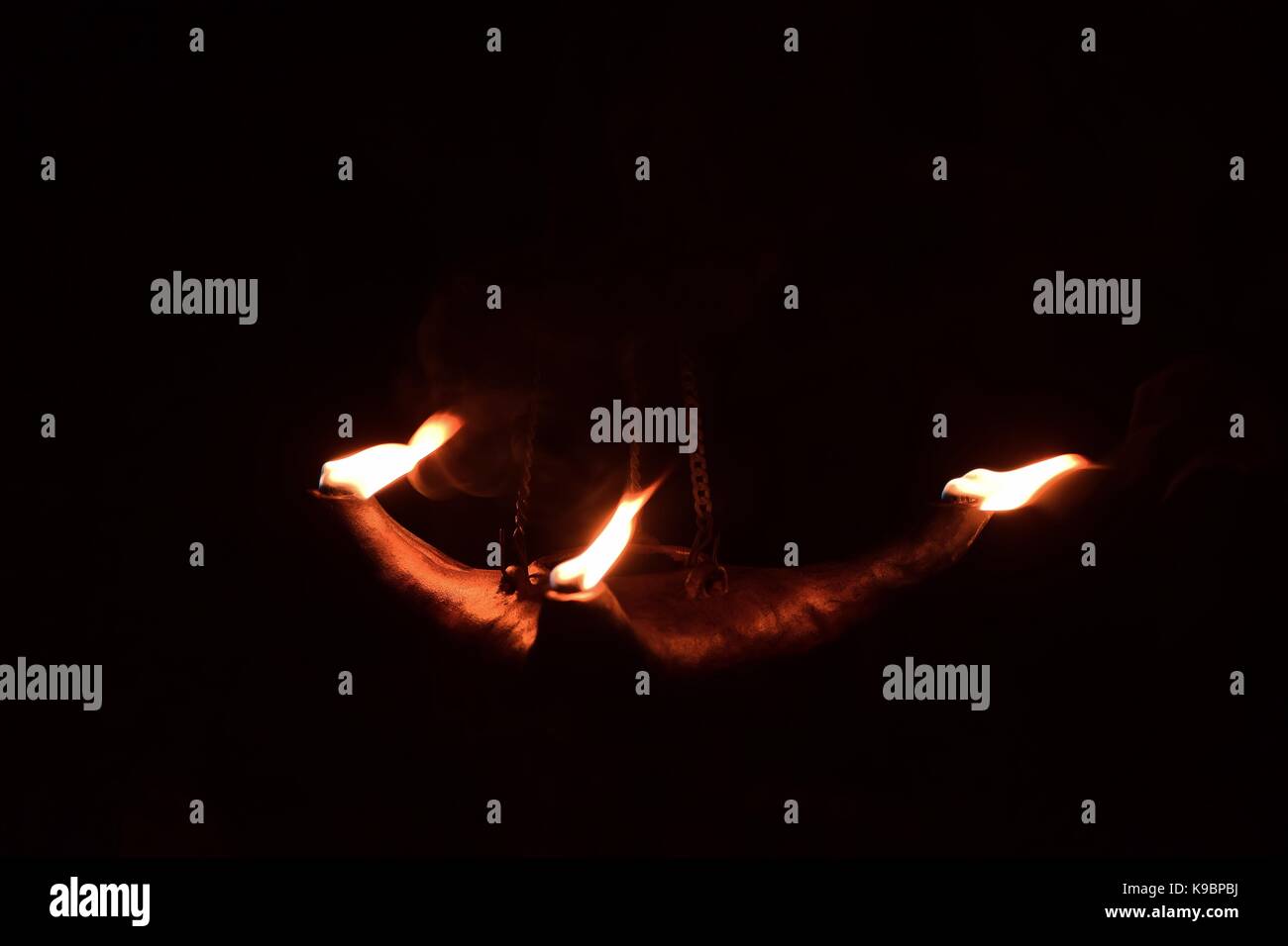 Tre fiamme in uscita di una argilla olio lampada, nel buio. La lampada è sospesa da una catena di metallo. Girato a Malta Foto Stock
