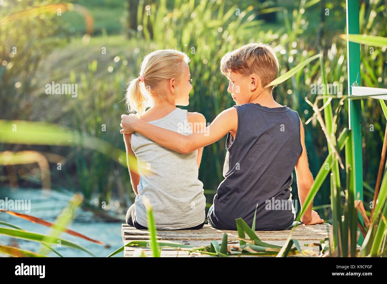 Estate in campagna. due bambini (di pari livello o migliori amici) seduto sul molo del lago. Foto Stock