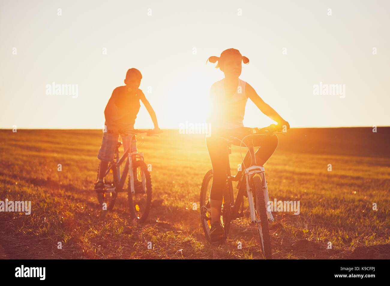 Ragazzo e una ragazza godendo in bicicletta al tramonto. Viaggio estivo in campagna. - Back lit Foto Stock