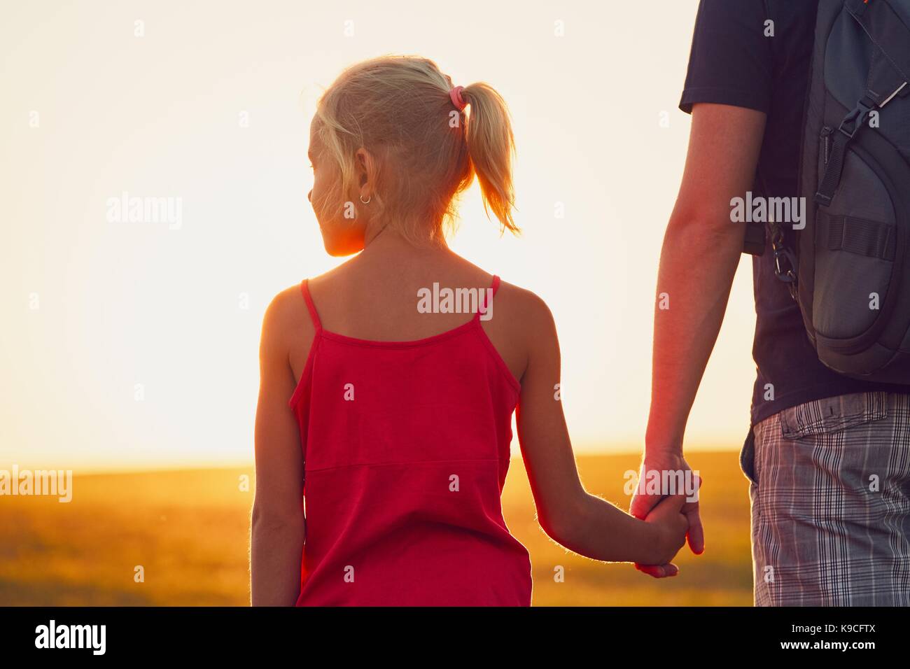 Viaggio estivo in campagna. ragazza con mano il suo padre al tramonto. - Back lit Foto Stock